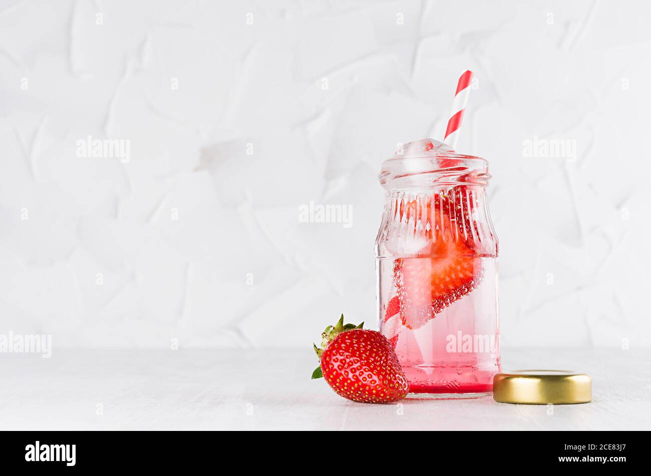 Joy helles frisches Sommergetränk mit roter Erdbeere, Stroh, Eis, Sodawasser, Kappe in elegantem Glas auf weichem hellen weißen Holztisch, Kopierraum. Stockfoto