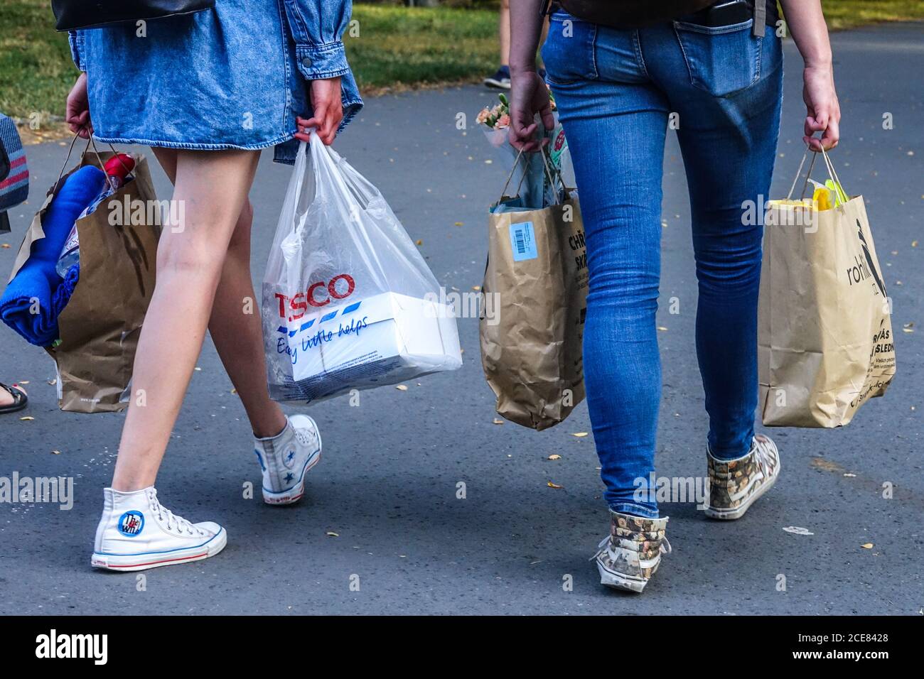 Zwei junge Frauen, die Einkaufstaschen aus dem Supermarkt tragen, eine Plastiktüte und Papiertüten zum Recycling, die zusammen weggehen Stockfoto