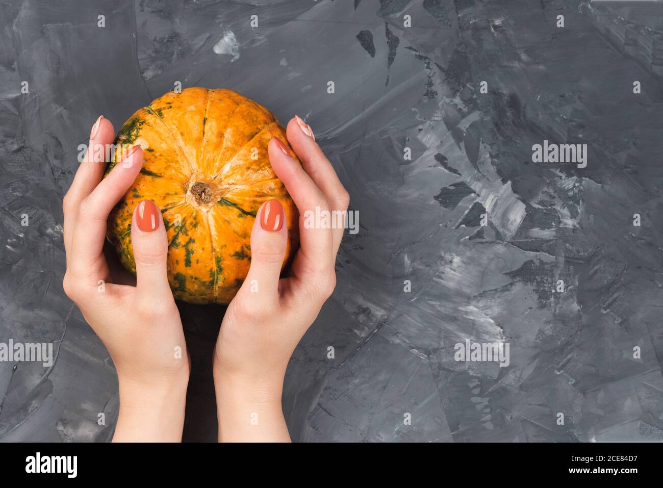 Frau hält einen Kürbis. Weibliche Hände mit trendigen Herbst Marmor Maniküre Stockfoto