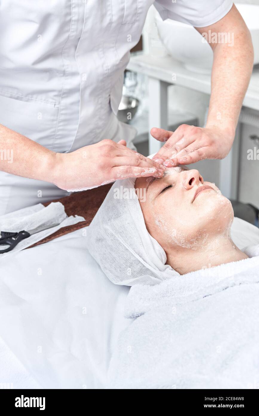 Männliche Kosmetikerin spendet Feuchtigkeit und reinigt sein Gesicht mit Sahne Seife. Frau in der Spa-Behandlungen Stockfoto