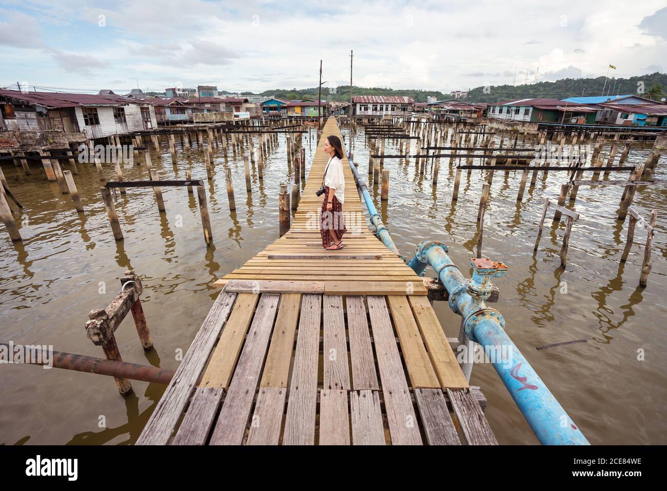 Seitenansicht der entzückenden ethnischen weiblichen Touristen, die sich am Kai entspannen In Kampong Ayer schwimmenden Dorf und wegschauen beim Genießen Urlaub in Bandar Seri Begawan Stockfoto