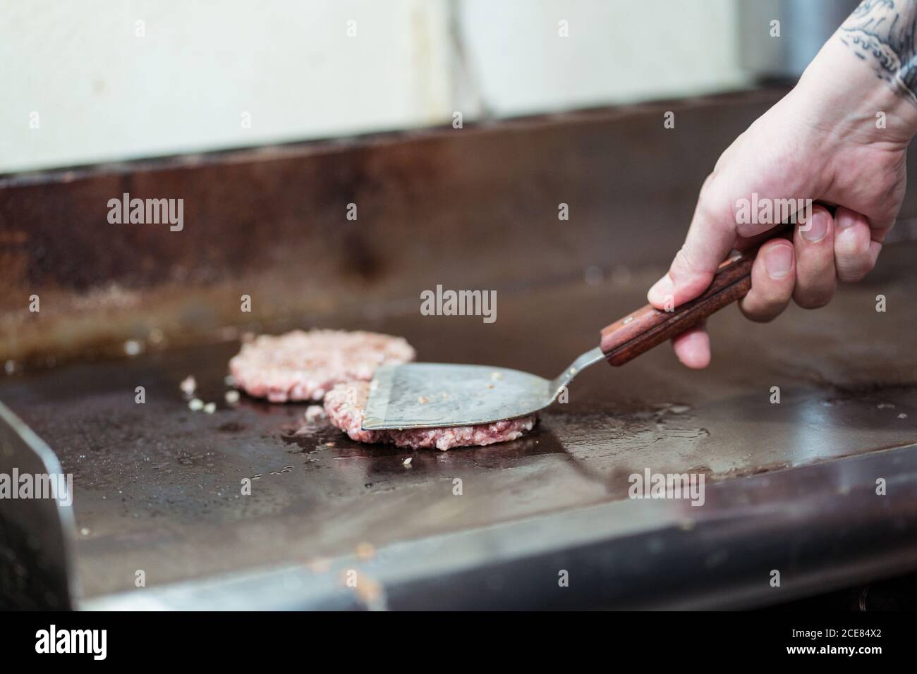 Unkenntlich Koch bereitet Koteletts aus Hackfleisch für Burger während Stehen am Herd mit Spachtel Stockfoto
