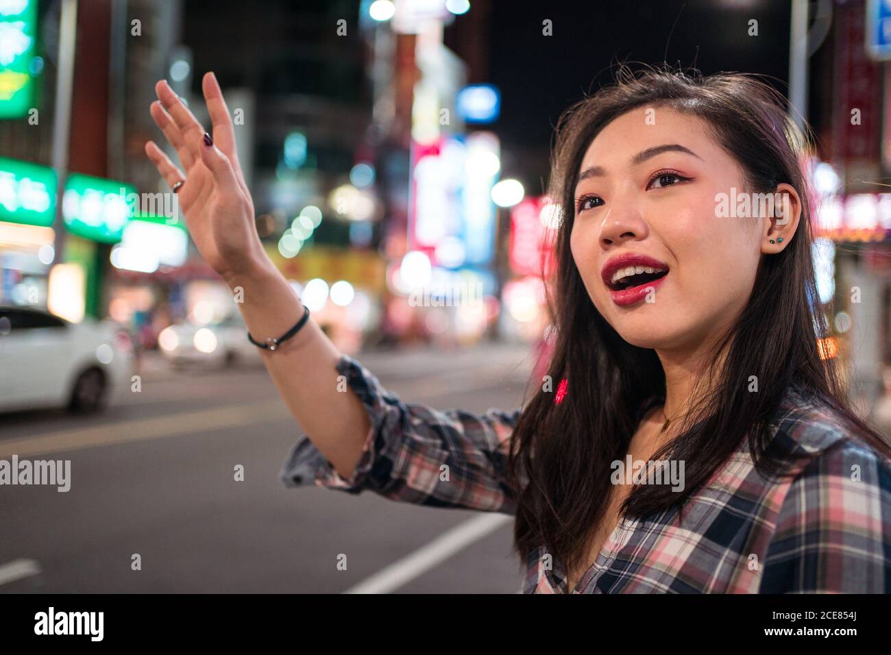 Seitenansicht der positiven jungen asiatischen Frau in Casual Wear Winkende Hand, während Sie nachts den Bus auf der Stadtstraße nehmen Zeit Stockfoto Seitenansicht der positiven jungen asiatischen Frau in Casual Wear Winkende Hand, während Sie nachts den Bus auf der Stadtstraße nehmen Zeit Stockfoto