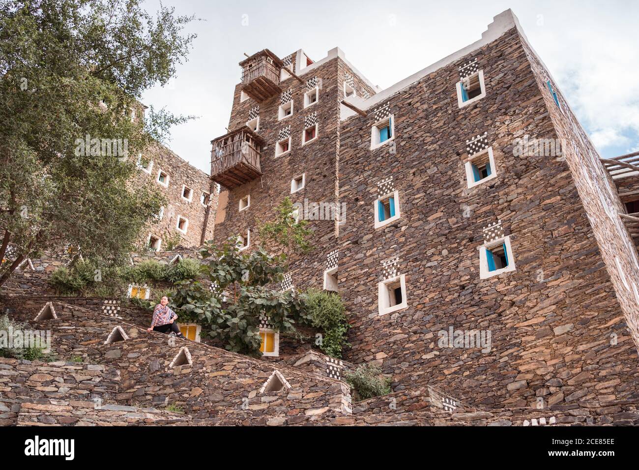 Weibliche Touristen sitzen auf dem Hintergrund von Steingebäuden mit bunten fenster während der Reise durch das Dorf Rijal Almaa in Saudi-Arabien Stockfoto