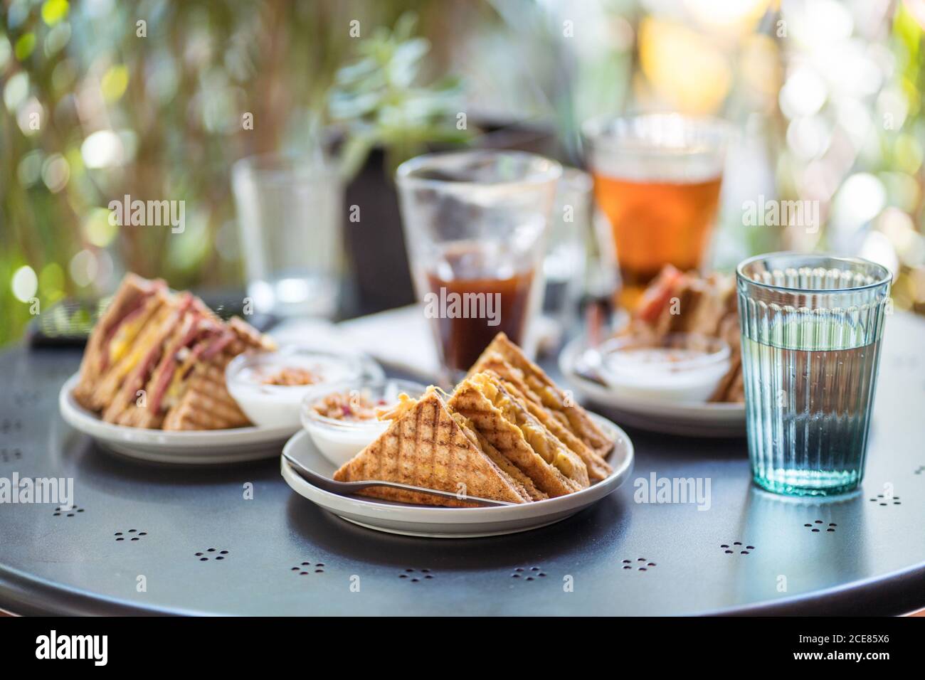 Köstliche Sandwiches auf dem Teller und erfrischende Getränke in Gläsern platziert Auf dem Tisch auf der Sommerterrasse des Cafés Stockfoto