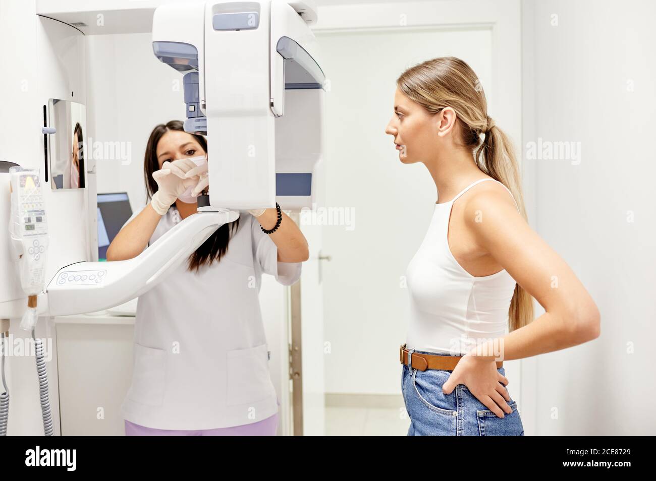 Blonde Frau mit den Händen auf der Taille wartet auf den Zahnarzt, um die Einstellungen des Röntgengeräts während des Termins in der modernen Zahnklinik anzupassen Stockfoto