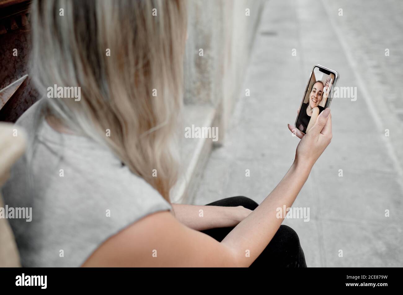 High-Angle-Cropped-Ansicht von unkenntlich junge Frau in casual Kleidung sitzt auf Steintreppe auf der Straße und genießen Video Gespräch mit einem Freund über das Smartphone Stockfoto