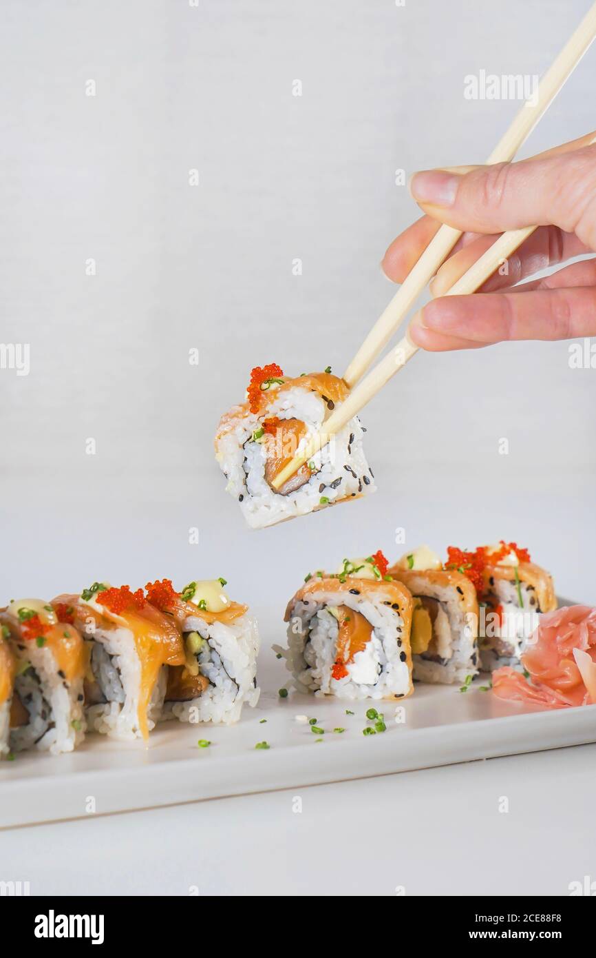 Von oben eine gesichtslose Frau, die Sushi mit Essstäbchen über dem weißen Holztisch hält Stockfoto