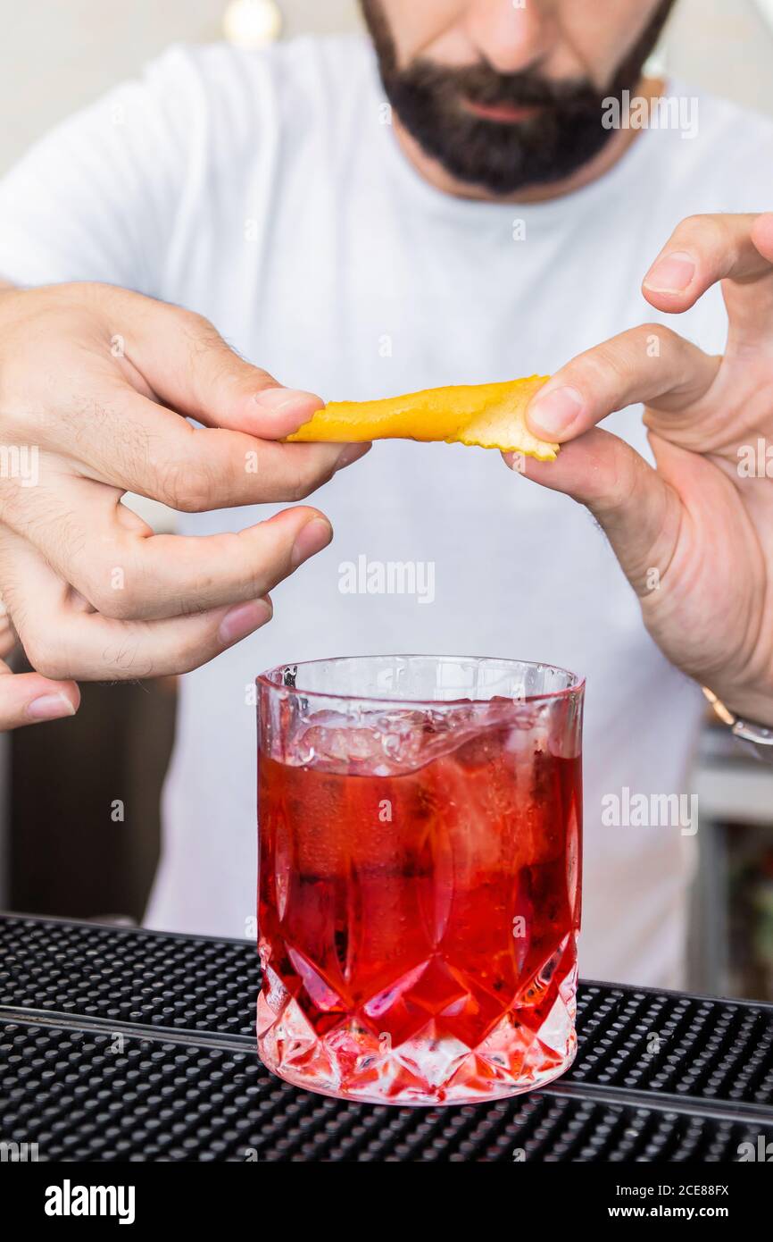 Der Barkeeper ohne Gesicht garniert einen altmodischen Cocktail aus Kristallglas Mit aromatischer Orangenschale Stockfoto