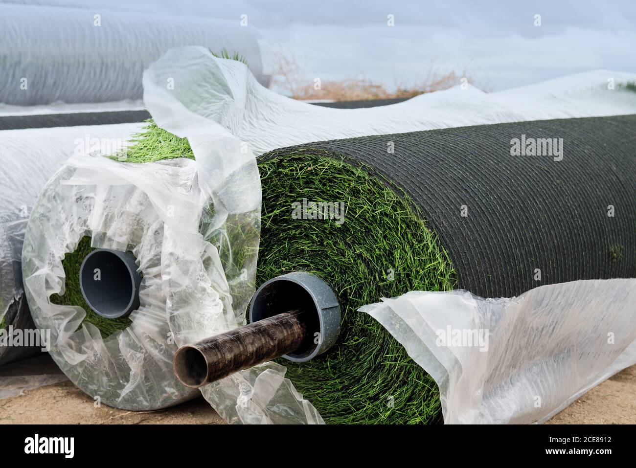 Rollen von grünen synthetischen Büschel in Kunststoff verpackt platziert Auf dem Boden auf dem Feld Stockfoto