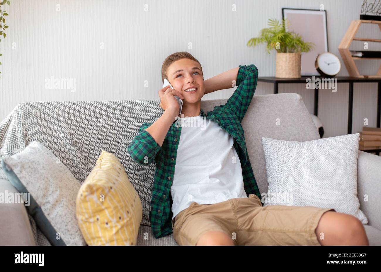 Sorgloser Teenager-Kerl, der am Telefon spricht, zu Hause sitzt Stockfoto