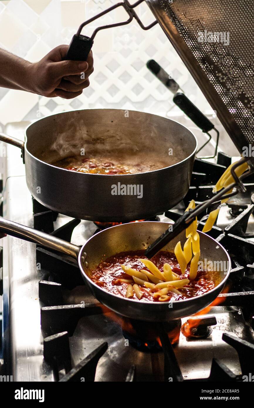 Unkenntlich kochen Spilling gekochte Pasta in Bratpfanne mit Tomaten Soße während der Arbeit in der Restaurantküche Stockfoto