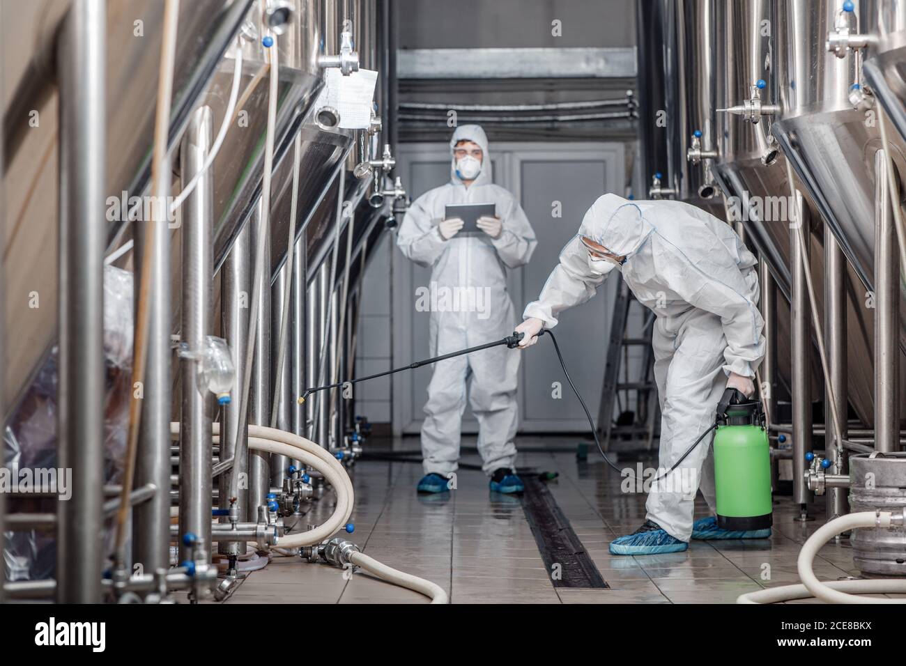 Produktqualität und Desinfektion. Männer in Hazmat Anzüge arbeiten mit Sprühtüten in der Bierfabrik Stockfoto