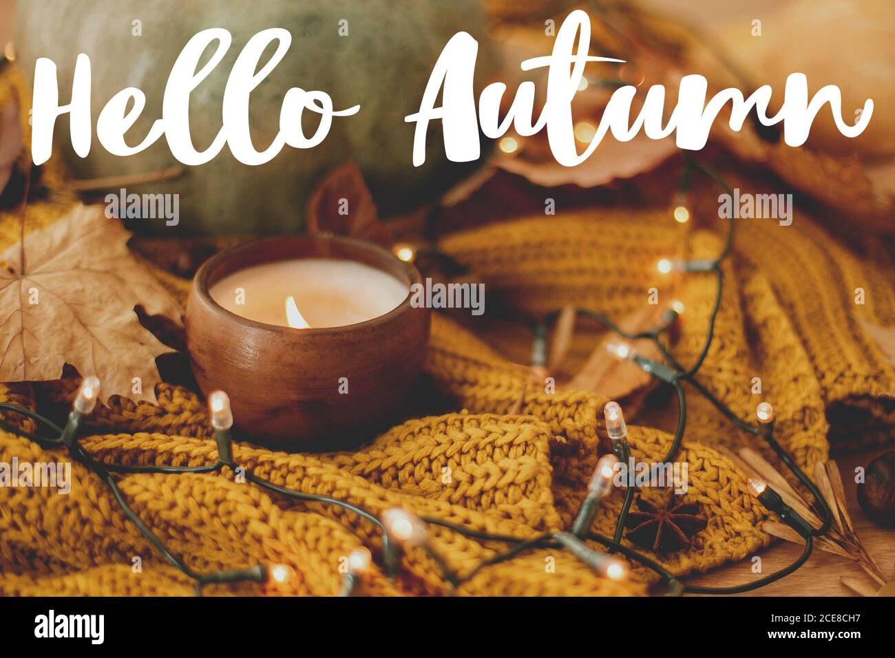 Hallo Herbst, handgeschriebener Text auf dem Hintergrund von Kürbis, Herbstblätter, Kerze, warme Lichter auf gelbem Strickpullover. Gemütlicher Herbst Stockfoto