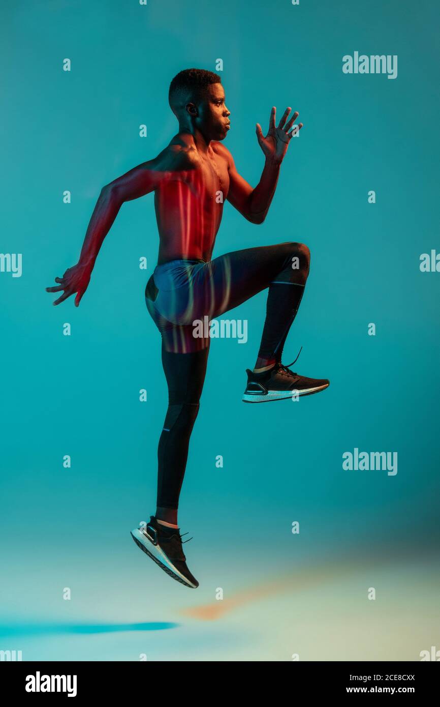 Ganzkörper-Seitenansicht des jungen afroamerikanischen männlichen Läufers  Im farbenfrohen Trainingsanzug sprintet man im Studio mit leuchtendem Neon  Beleuchtung Stockfotografie - Alamy