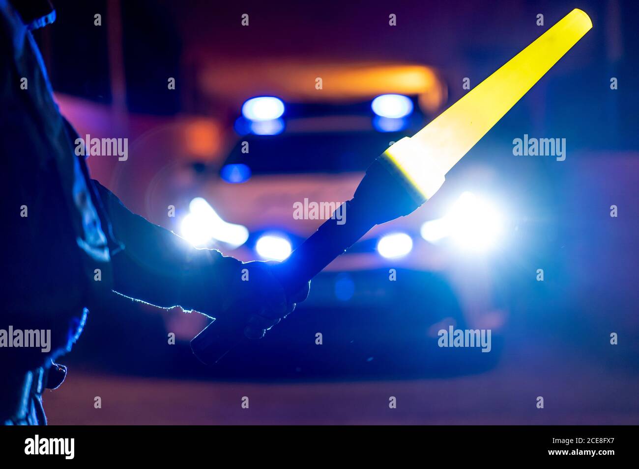 Rückansicht des Getreidepoliziers stehend mit beleuchtetem Verkehr Zauberstab vor dem Streifenwagen mit Blinklicht an Nacht Stockfoto