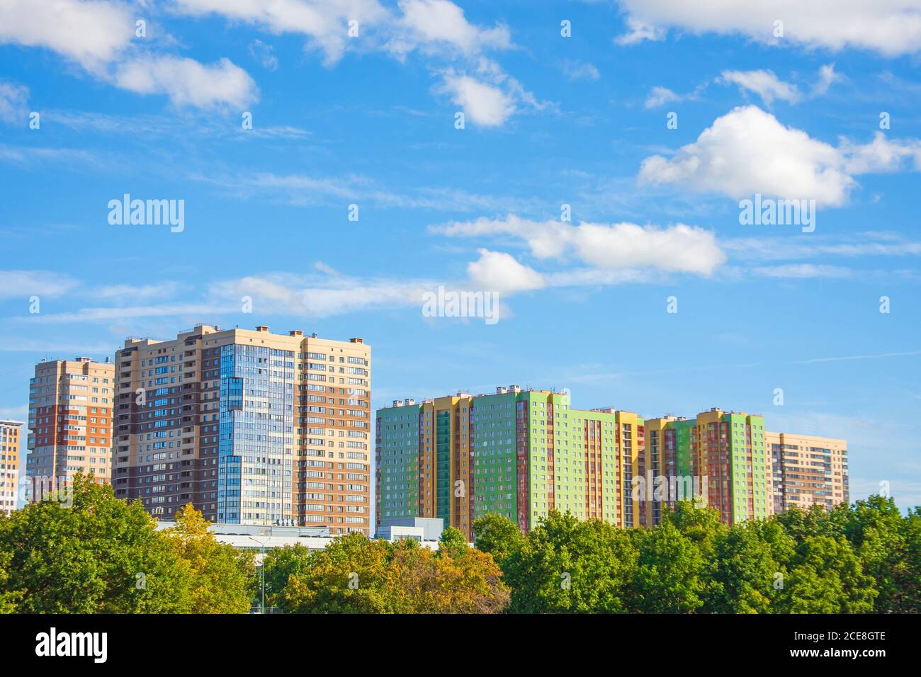 Grüner Sommerpark mit jungen Eichen und Weiden. Im Hintergrund mehrstöckige Wohngebäude in einer ökologisch sauberen Gegend für die Bevölkerung Stockfoto