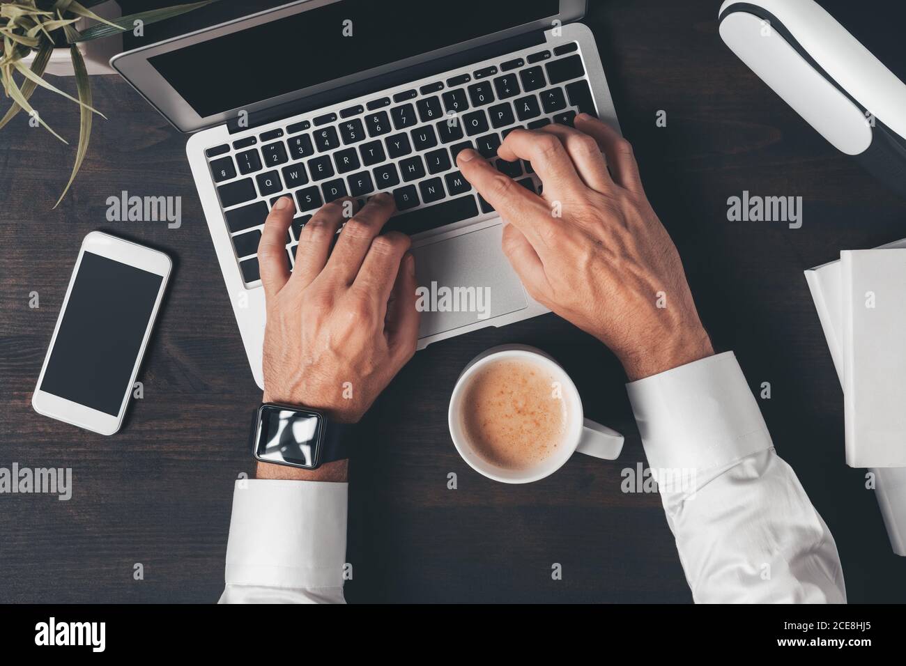 Draufsicht auf die Hände eines Geschäftsreisenden, der die Tastatur eines Laptops mit einer Tasse Kaffee auf dem Schreibtisch tippt, Ansicht des Arbeitsbereichs von oben Stockfoto