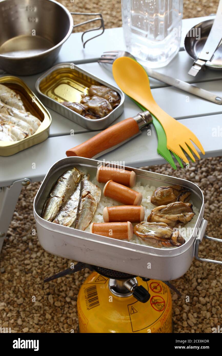 Camping Kochen. Geölte Sardinen, Würste und geräucherte Austern auf gekochtem Reis in Messdose. Stockfoto