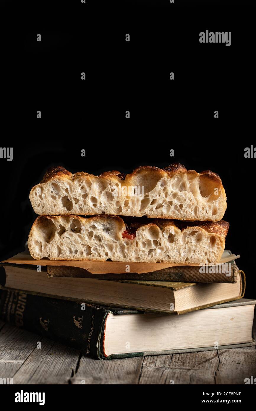 Stücke von traditionellen italienischen Brot Focaccia mit Gemüse auf gelegt Stapel alter Bücher auf schwarzem Hintergrund Stockfoto
