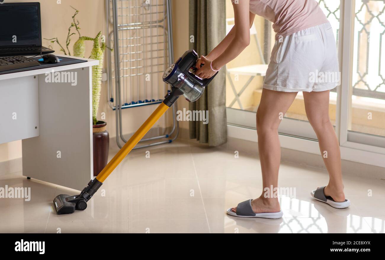 Frau, die das Wohnzimmer mit einem kabellosen Staubsauger saugt. Hausreinigung und Wartung abstrakt Stockfoto