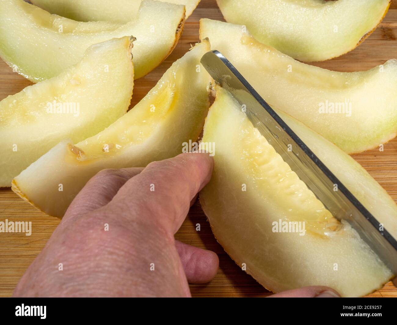 Nahaufnahme der Hände eines Mannes, der einen Teil einer saftigen Melone hält, während er ein scharfes gezacktes Stahlmesser verwendet, um es in Segmente zu schneiden. Stockfoto