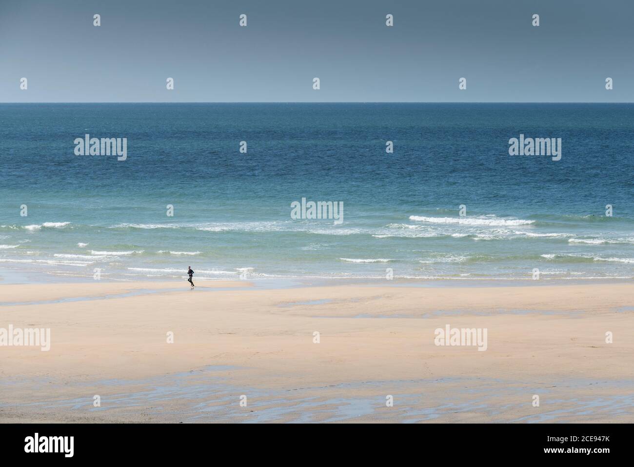 Eine einköpfige Person, die am Fistral Beach in Newquay in Cornwall entlang der Küste läuft. Stockfoto