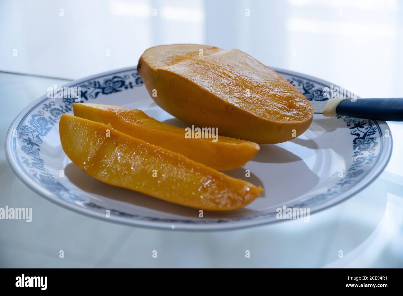 Eine frisch geschnittene Mango mit selektivem Fokus wird auf einen Teller gelegt und fertig zum Mango mit dem verschwommenen weißen Hintergrund. Stockfoto