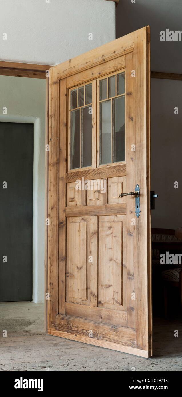 Eine alte Kastenholztür mit Fenstern aus unbehandeltem Fichtenholz steht offen in einen Raum. Stockfoto