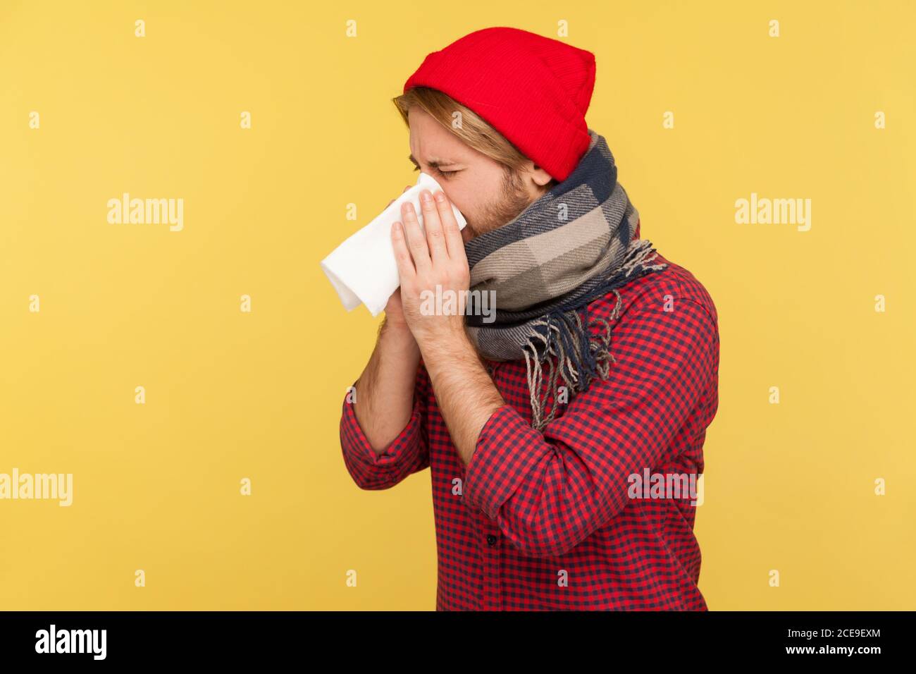 Kranker Mann mit Hut und warmem Schal hustet Niesen Gewebe, Gefühl unwohl mit laufender Nase, Halsschmerzen, leiden Allergie oder saisonale Grippe-Symptome Stockfoto
