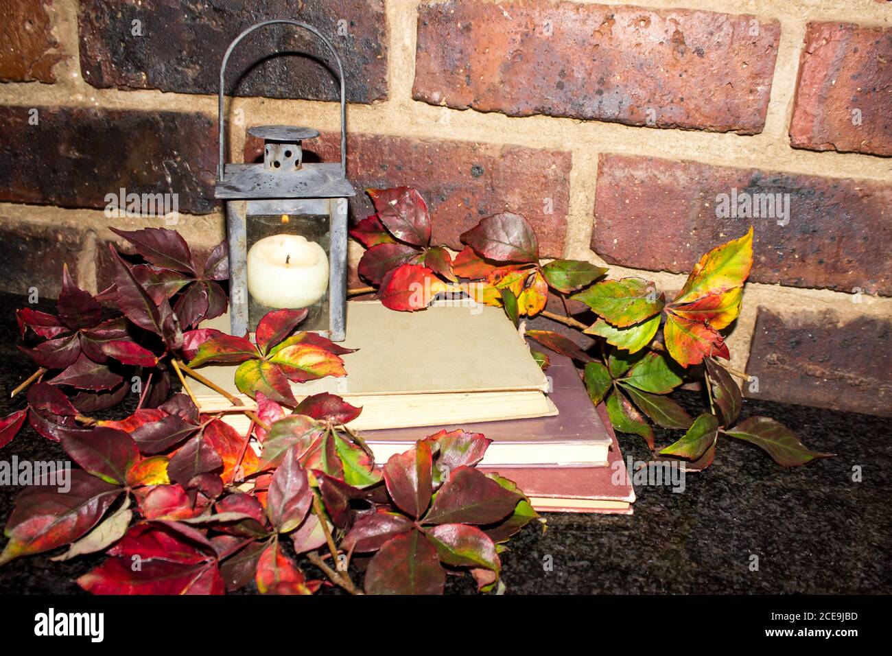 Ein vom Herbst inspiriertes Stillleben, bestehend aus einem Stapel von Drei Bücher und ein Laterne geformter Kerzenhalter umgeben von Die bunten Blätter eines Virginia Stockfoto