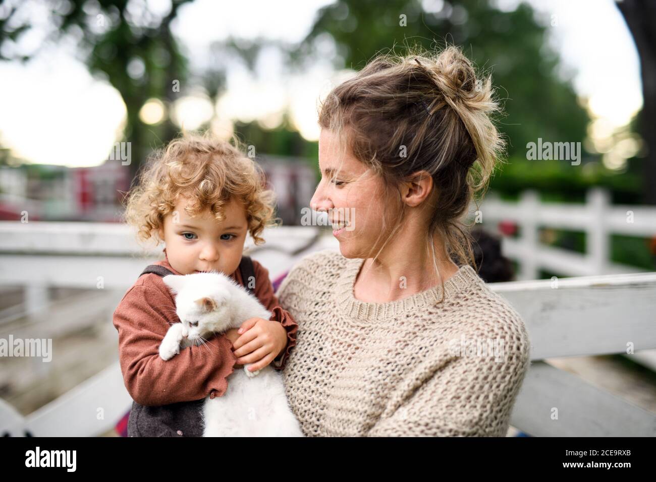 Kleines Mädchen mit Mutter, die auf dem Bauernhof steht und mit der Katze spielt. Stockfoto