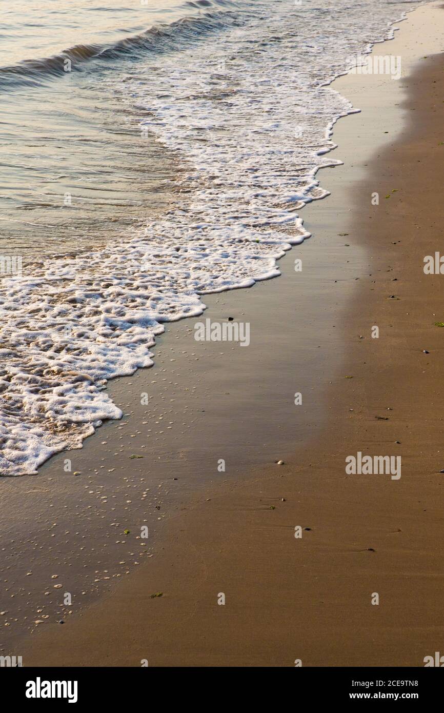 Kleine Wellen und Wellen an einem goldenen Sandstrand. Frühe Morgensonne Stockfoto