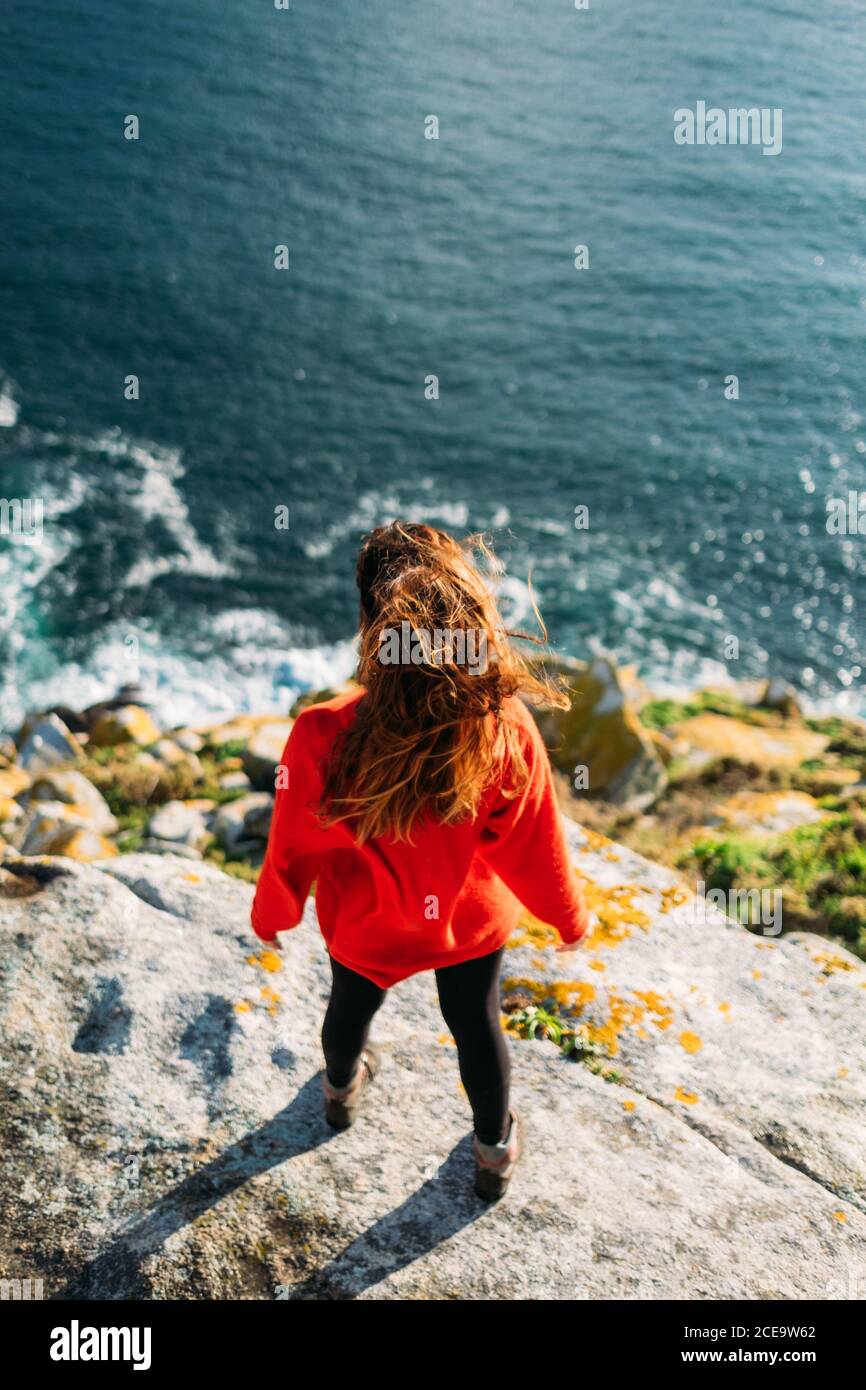 Rückansicht eines Weibchens, das am Rand steht und auf das Meer blickt. Vertikale Außenaufnahme. Stockfoto