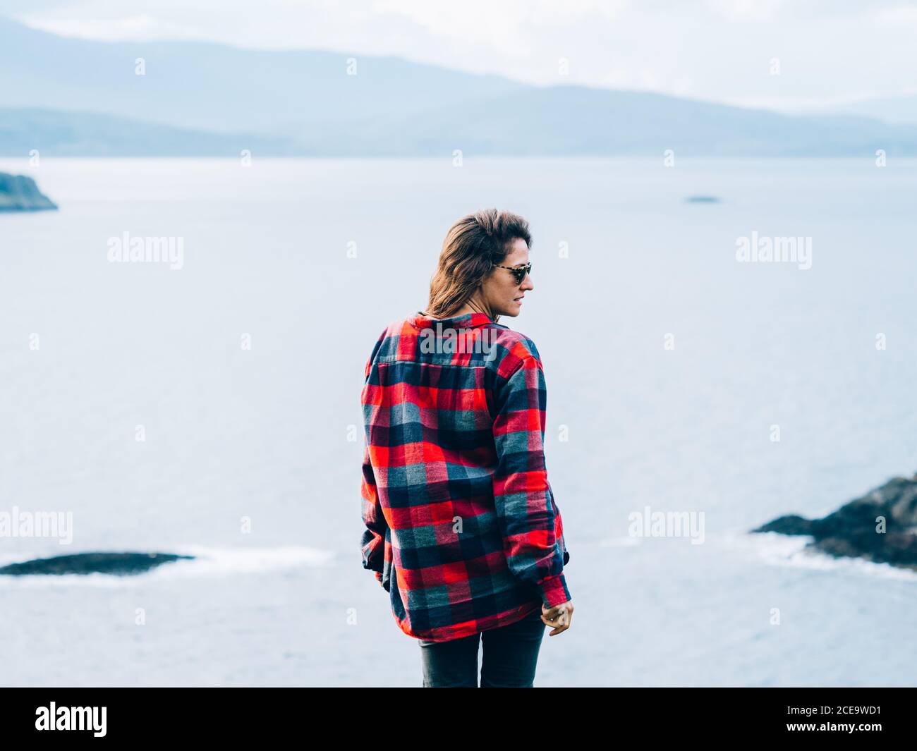 Rückansicht einer Frau in kariertem Hemd und Sonnenbrille, die gegen die Küste in Highlands, Schottland, steht. DIGITALKAMERA OLYMPUS Stockfoto