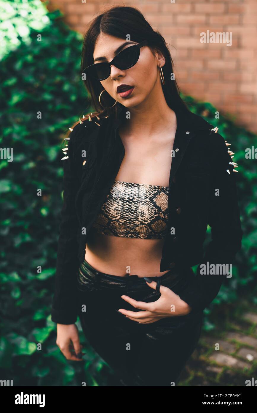 Junge Dame im Crop Top und schwarze Samtjacke mit Silberdornen mit rotem Lippenstift und Ohrringen Stockfoto