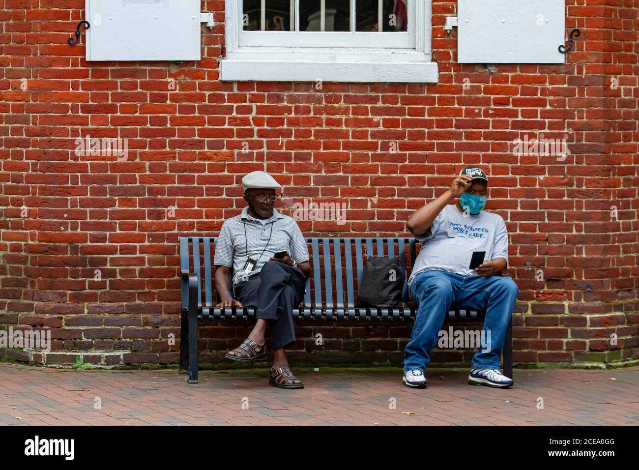 Annapolis, MD 08/21/2020: Zwei ältere afroamerikanische Männer sitzen auf einer Bank vor einem alten Backsteingebäude in Annapolis. Einer trägt Gesichtsmaske fällig Stockfoto