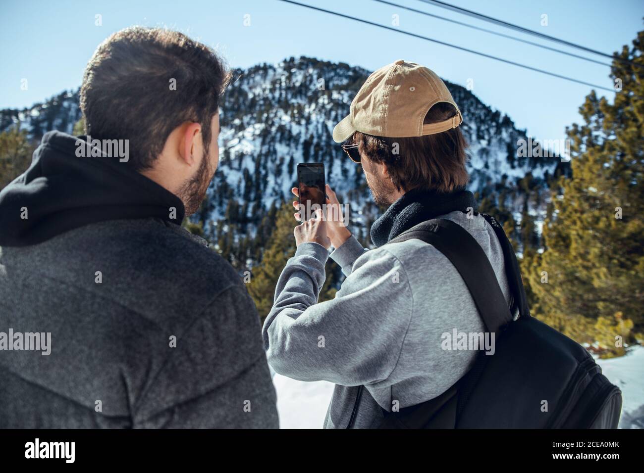 Rückansicht von jungen Fotografen mit professioneller Kamera und Handy stehen zwischen Bergen im Schnee in Cerdanya, Frankreich Stockfoto