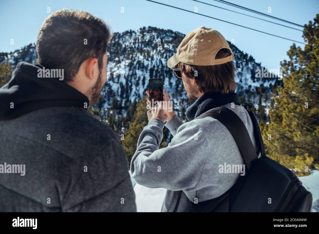 Rückansicht von jungen Fotografen mit professioneller Kamera und Handy stehen zwischen Bergen im Schnee in Cerdanya, Frankreich Stockfoto