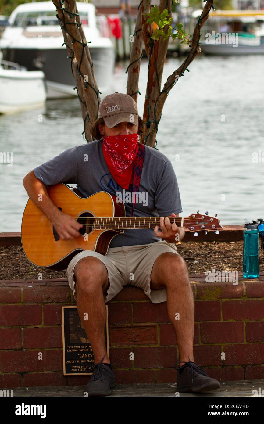 Annapolis, MD 08/21/2020: Ein junger Kaukasusmann sitzt auf einer Ziegelmauer in Annapolis Marina und spielt klassische Gitarre. Dieser Straßenmusiker ist w Stockfoto