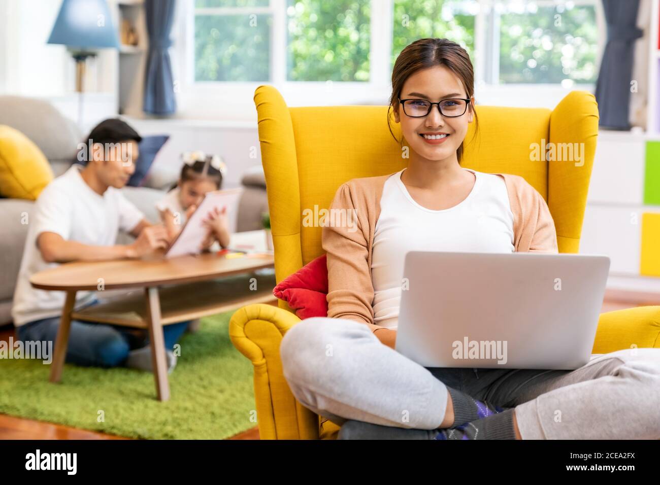 Asiatische arbeiten Mutter Arbeit von zu Hause in Wohnzimmer mit Hintergrund von Vater und Tochter lesen Geschichte Buch während Stadt Lockdown. Diversity-Konzept Stockfoto