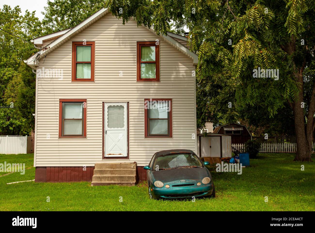 Chesapeake City, MD, USA 08/25/2020: Ein altes kaputtes rostiges Auto mit nebligen Scheinwerfern wird vor einem Einfamilienhaus mit großem Hof zurückgelassen. Das ist es Stockfoto