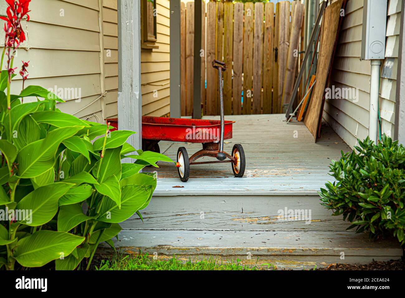 Ein roter alter rostiger Spielzeugwagen wurde an der Tür eines alten Hauses zurückgelassen. Die hölzerne Veranda das Spielzeug wurde links hat graue Farbe, die Zeichen des Alterns zeigt. Dort Stockfoto