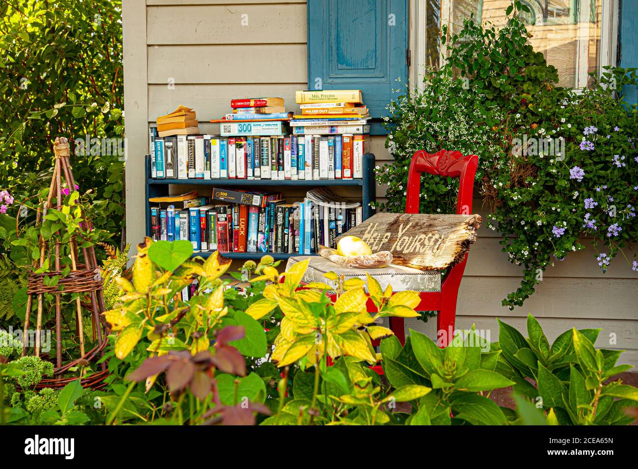 Chesapeake City, MD, USA 08/25/2020: Ein Bücherregal voller Bücher verschiedener Genres befindet sich auf der Veranda eines alten Hauses. Ein Schild mit der Aufschrift „Hilf dir Stockfoto