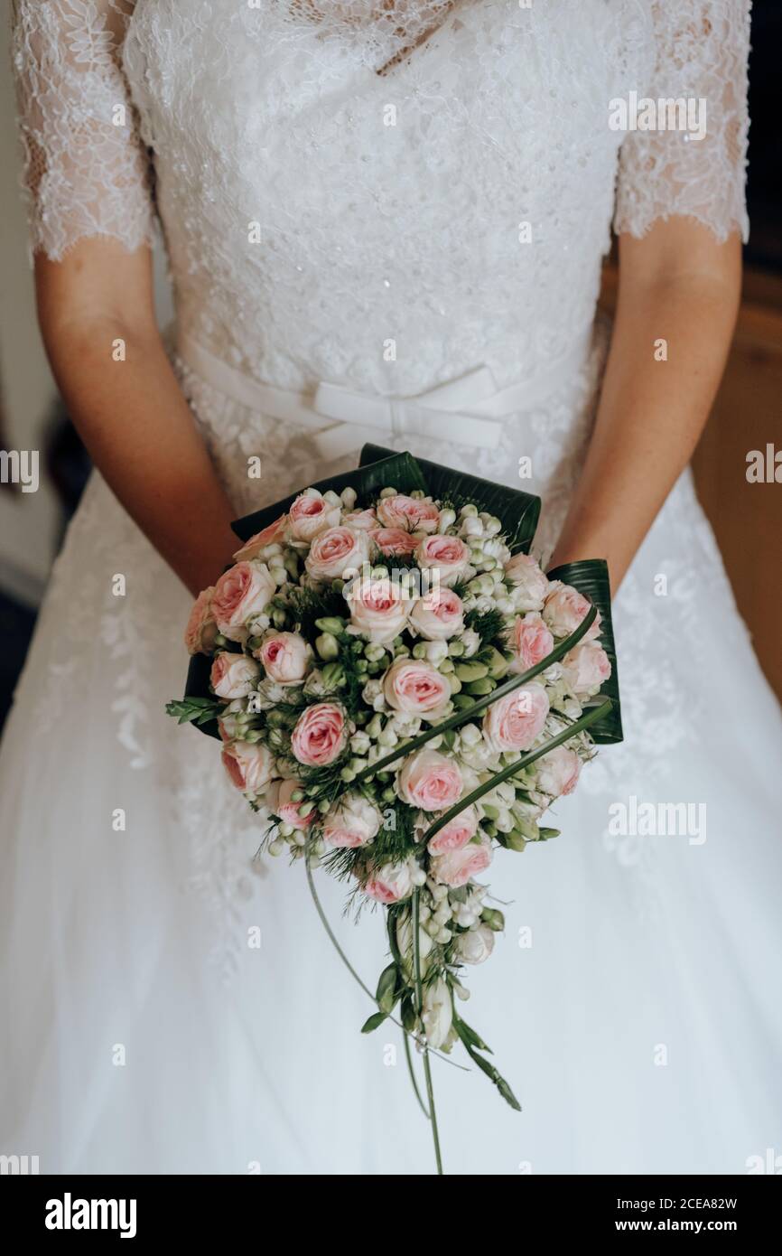 Crop Frau in Spitze Brautkleid hält schöne grüne Bouquet mit rosa Rosen Stockfoto