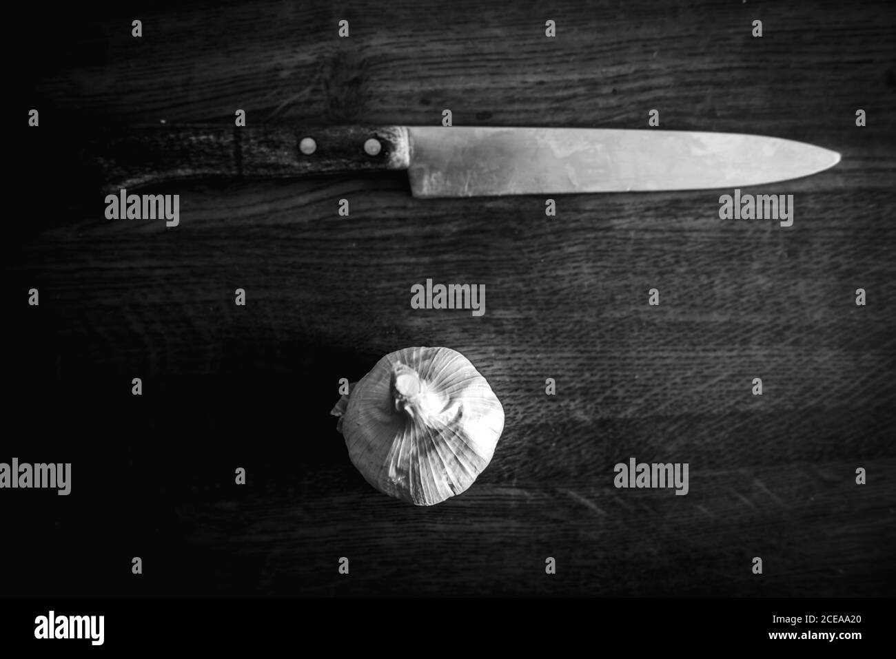 Schwarz und weiß von oben Schuss des scharfen Messers und Knoblauchkopf auf Holztisch Stockfoto