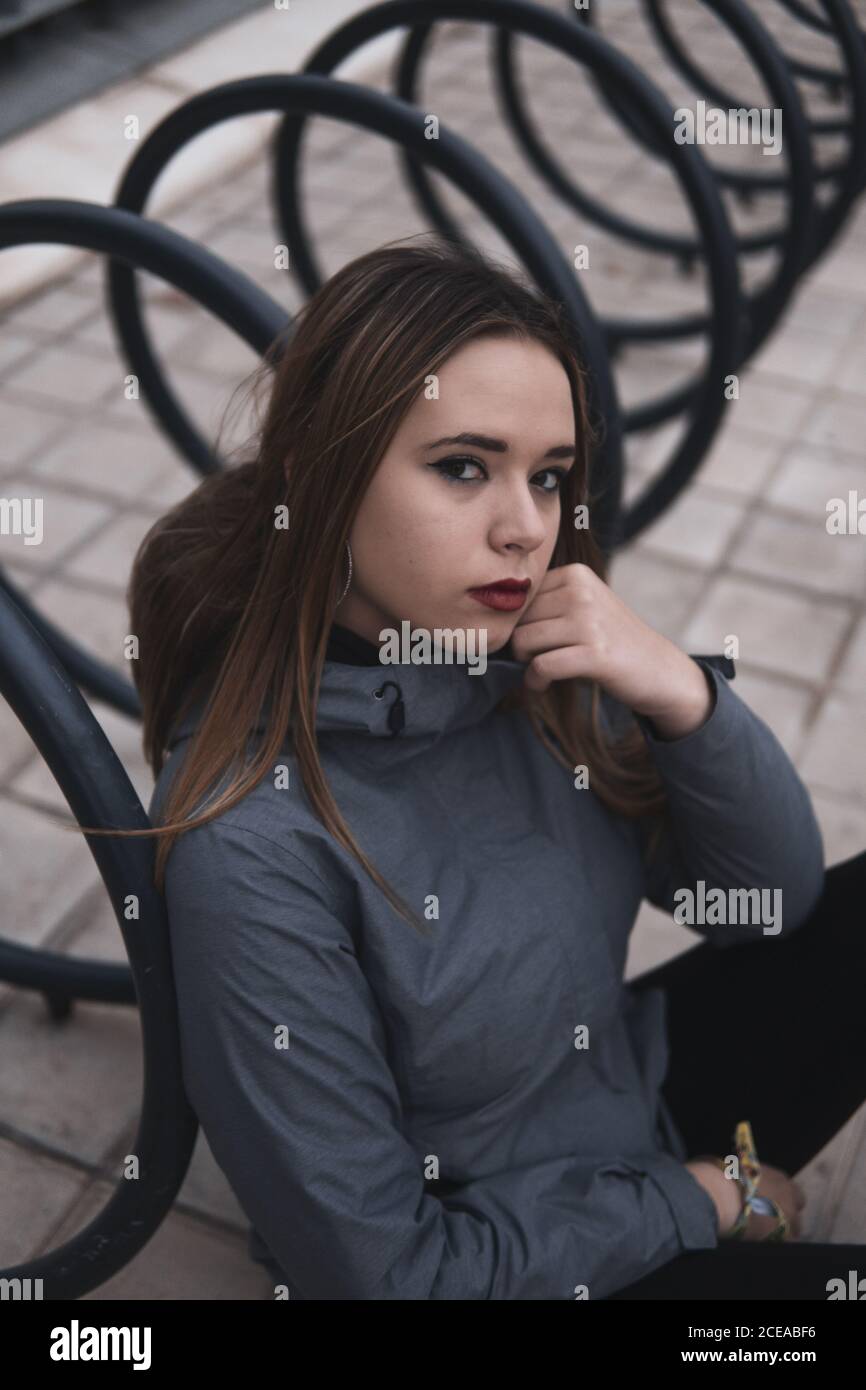 Charmante Frau in Mantel und Leggins sitzen in der Nähe Parkplatz für Fahrräder Stockfoto