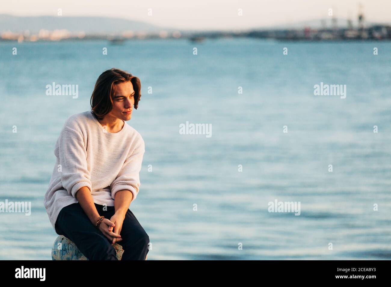 Thinking schöner Mann in Freizeitkleidung sitzt in der Nähe Wasseroberfläche An sonnigen Tag Stockfoto