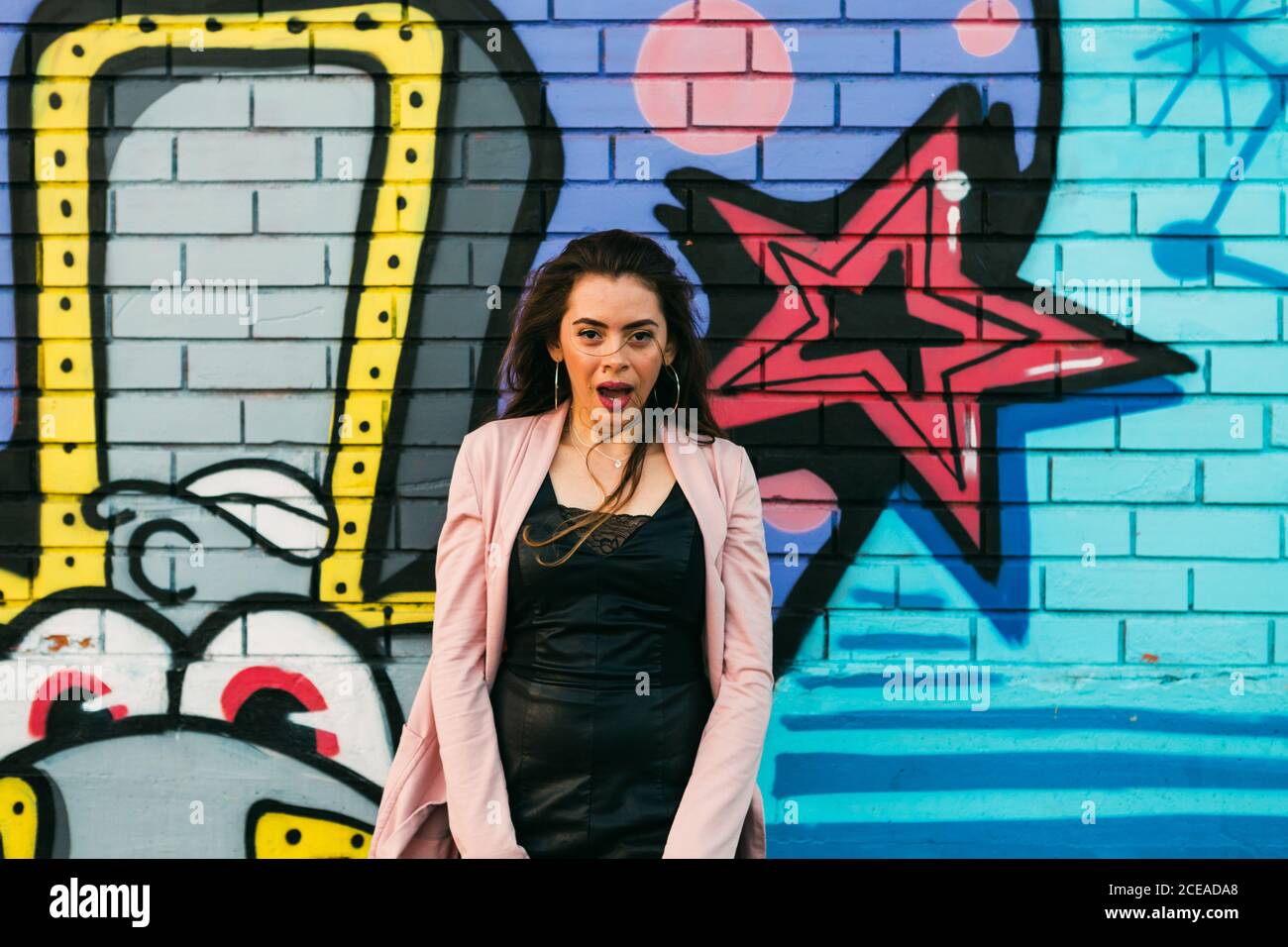 Junge lächelnde Frau in legerer Kleidung in der Nähe der Graffiti-Wand Stockfoto