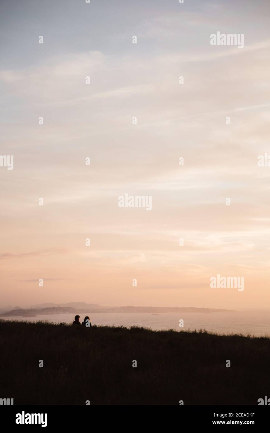 Rückansicht von Jungs sitzen auf Gras und Blick malerischen Sonnenuntergang am Himmel Hintergrund in Kantabrien, Spanien Stockfoto